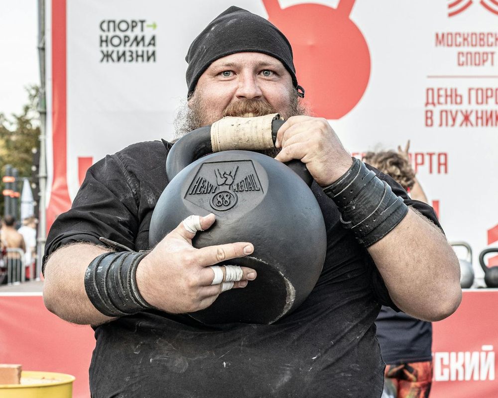Male athlete performing rhythmic kettlebell swing in a dark studio